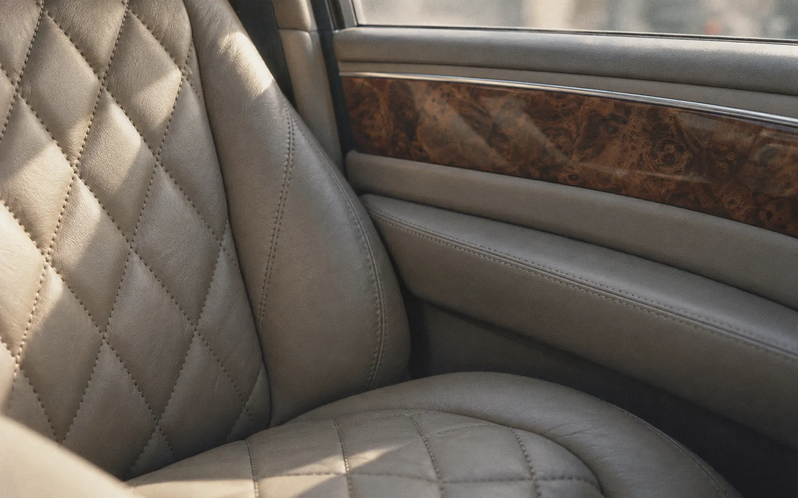Illustration of quilted leather seat stitching beside a burr-walnut door trim